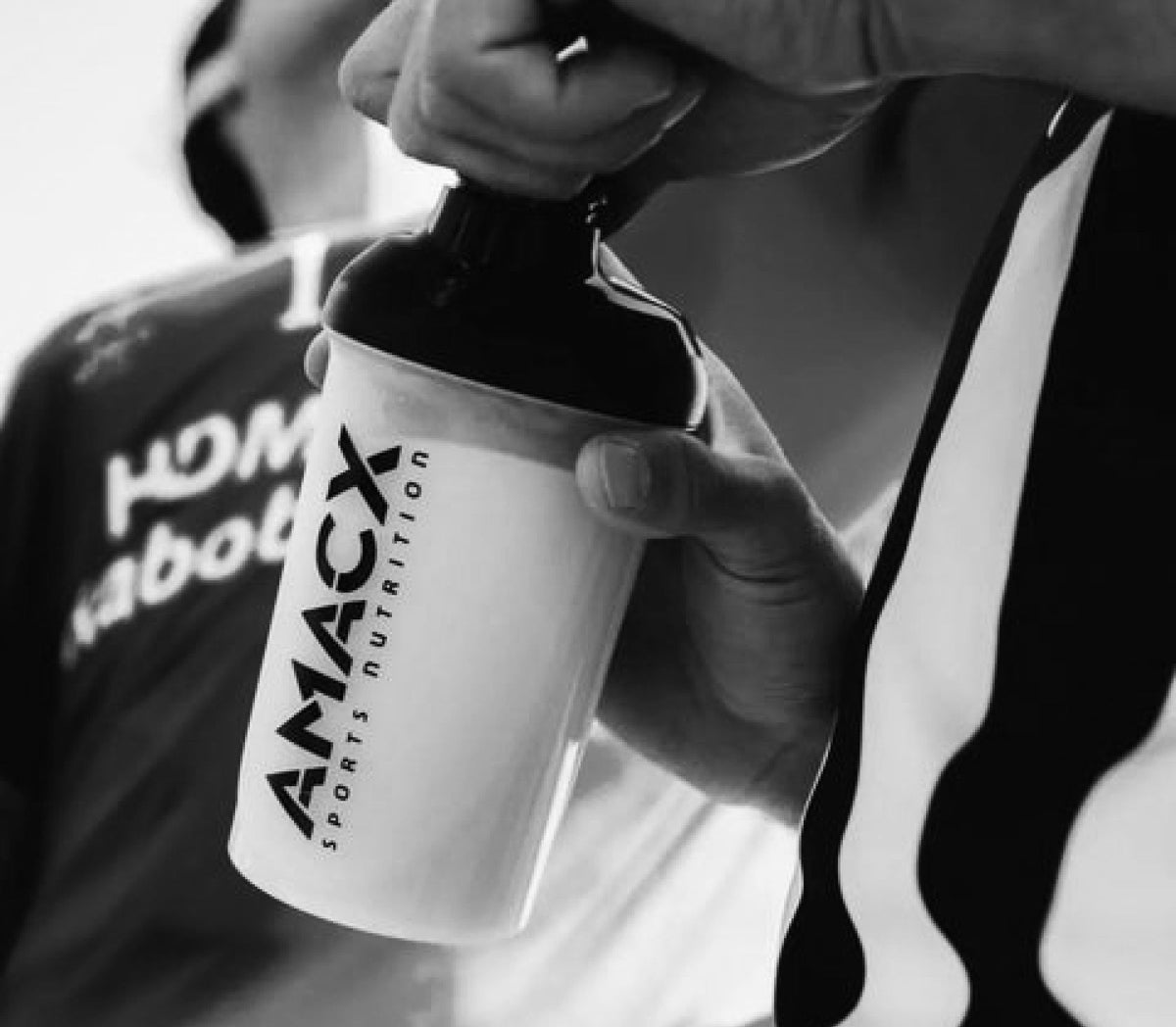 Hand houdt een Amacx-shaker vast naast een wielrenner, zwart-witfoto